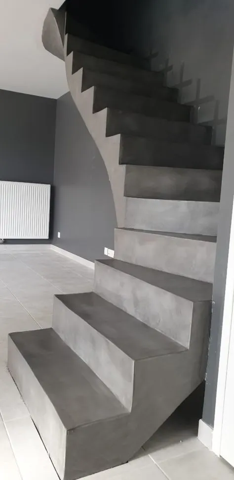 Escalier quart tournant en béton ciré gris avec marches, contremarches et limon courbe traités d'un seul tenant
