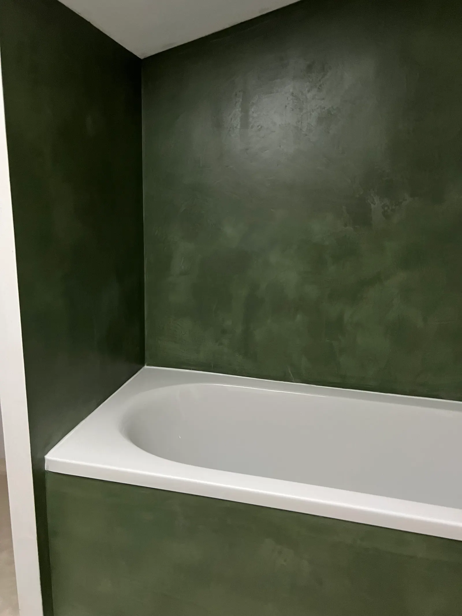 Murs et tablier de baignoire en béton ciré vert profond, vus avant la pose du pare-baignoire