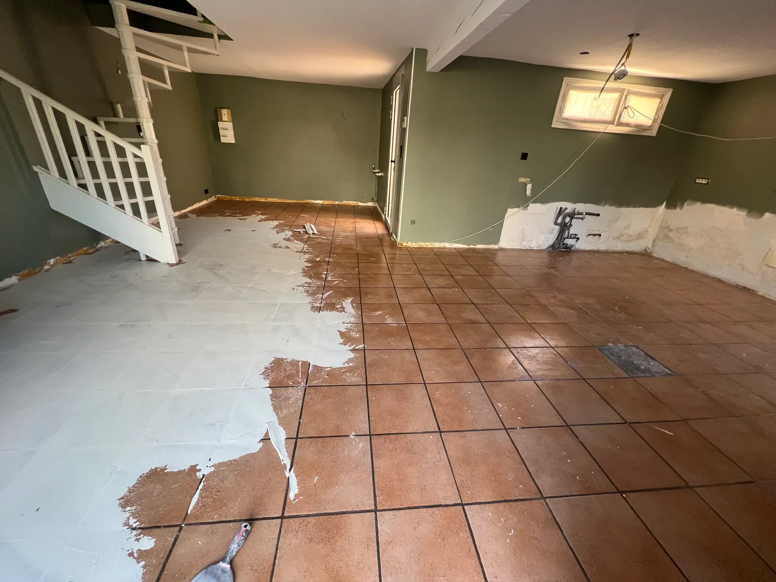 La même pièce avant travaux : carrelage en terre cuite en partie recouvert d'une première couche claire