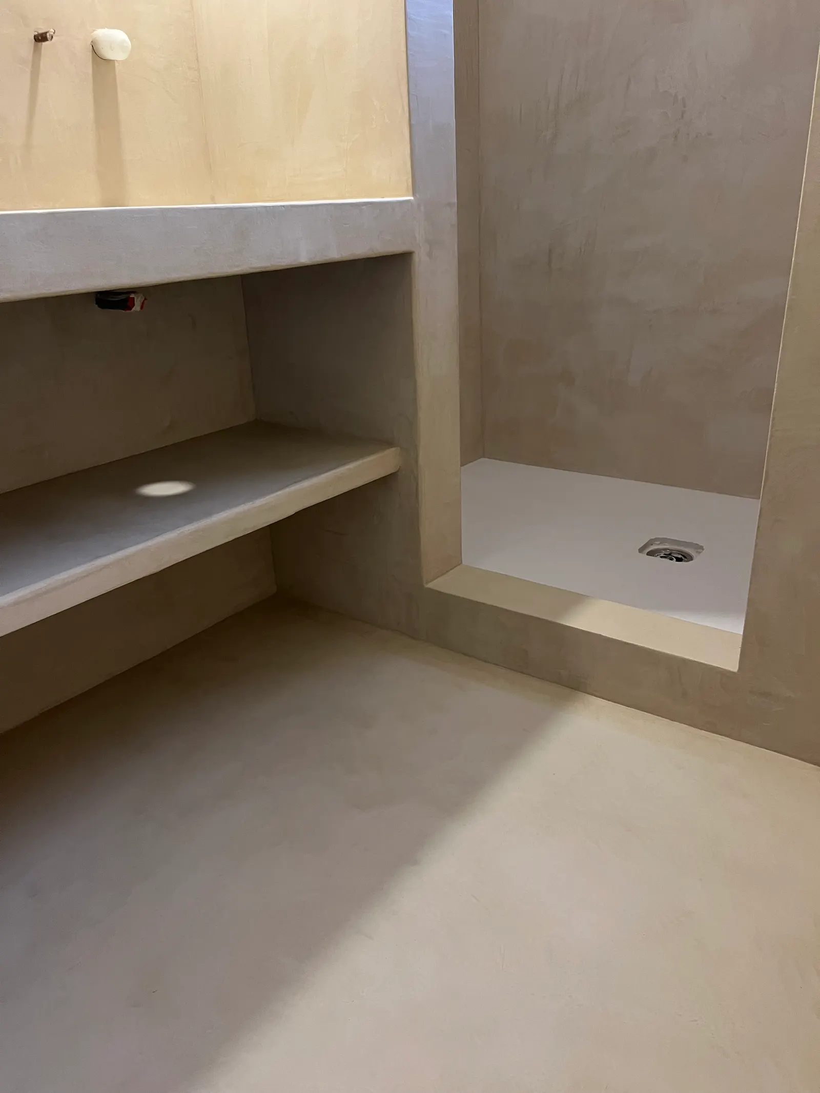 Sol, meuble maçonné et entrée de douche en béton ciré sable, vus avant la pose des vasques