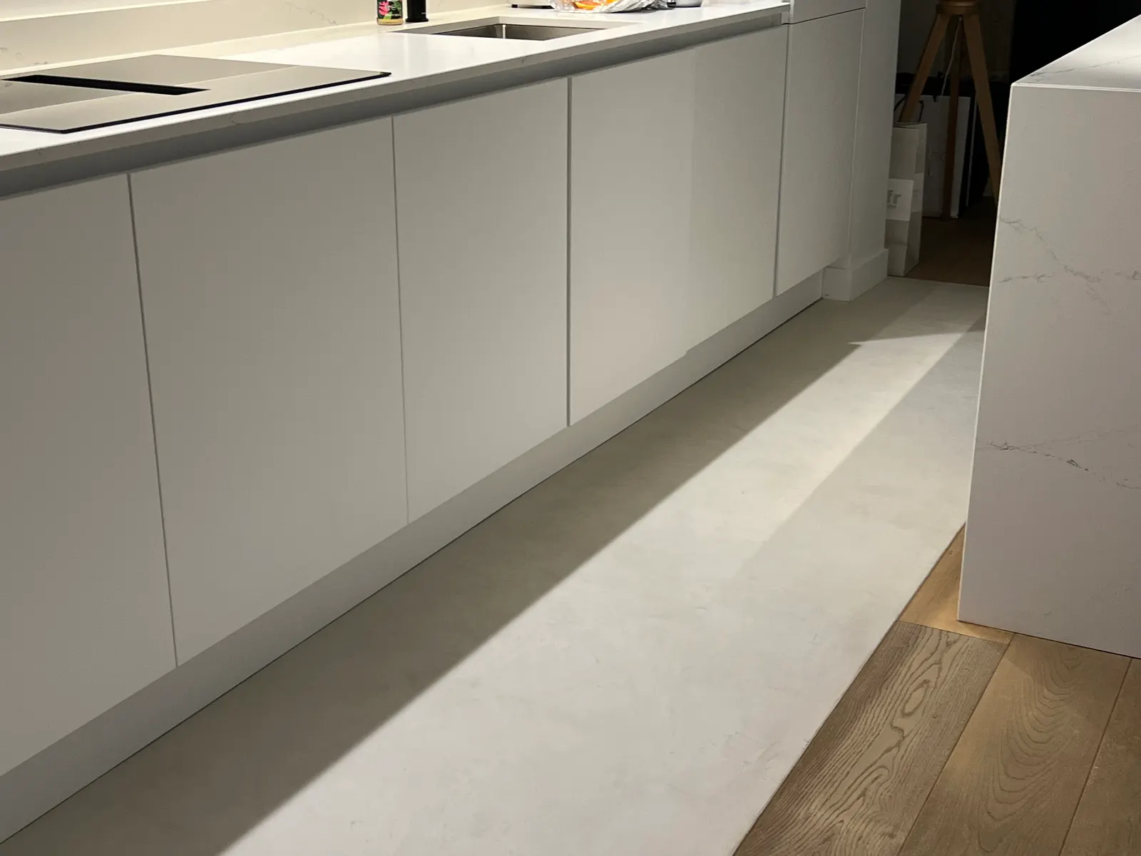 Jonction nette entre le béton ciré blanc du sol de cuisine et le parquet en chêne, au pied d'un îlot