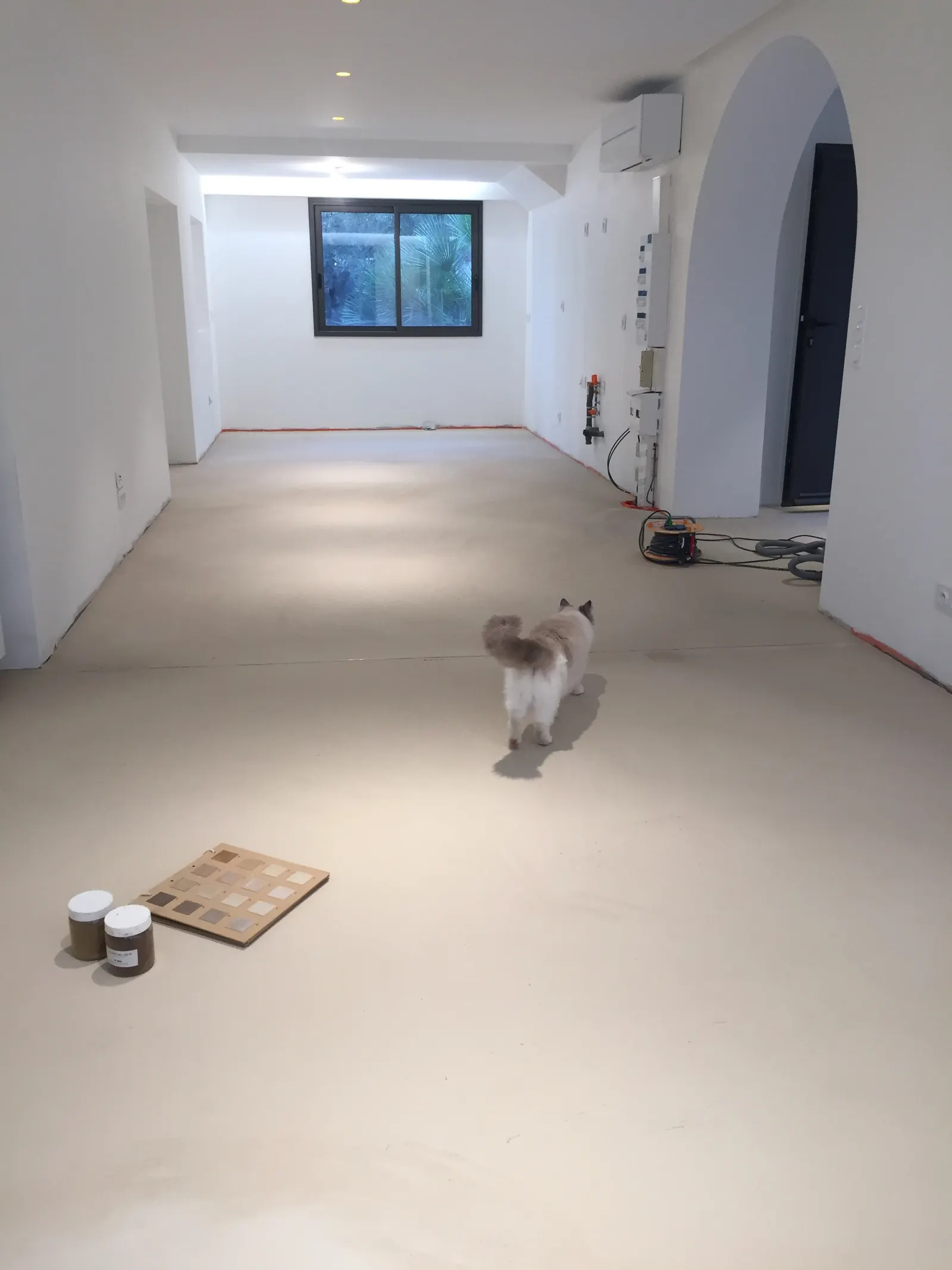 Grande pièce blanche avec un sol en béton ciré beige, un nuancier de teintes et des pots d'échantillons posés au sol