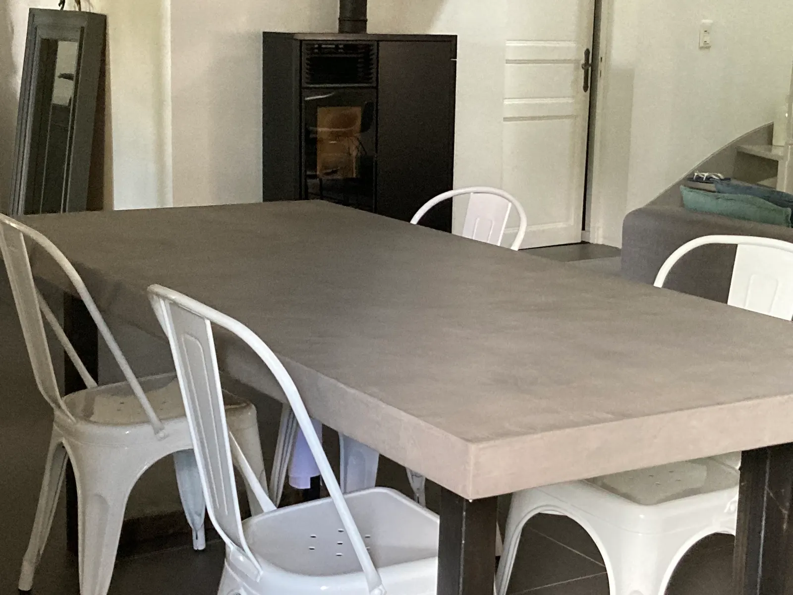 Table de salle à manger avec plateau épais en béton ciré gris taupe, entourée de chaises métalliques blanches