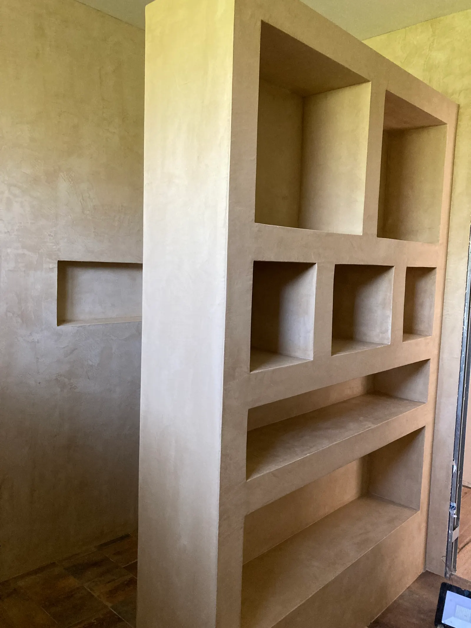Bibliothèque maçonnée beige en claustra et mur voisin avec niche, tous deux en béton ciré