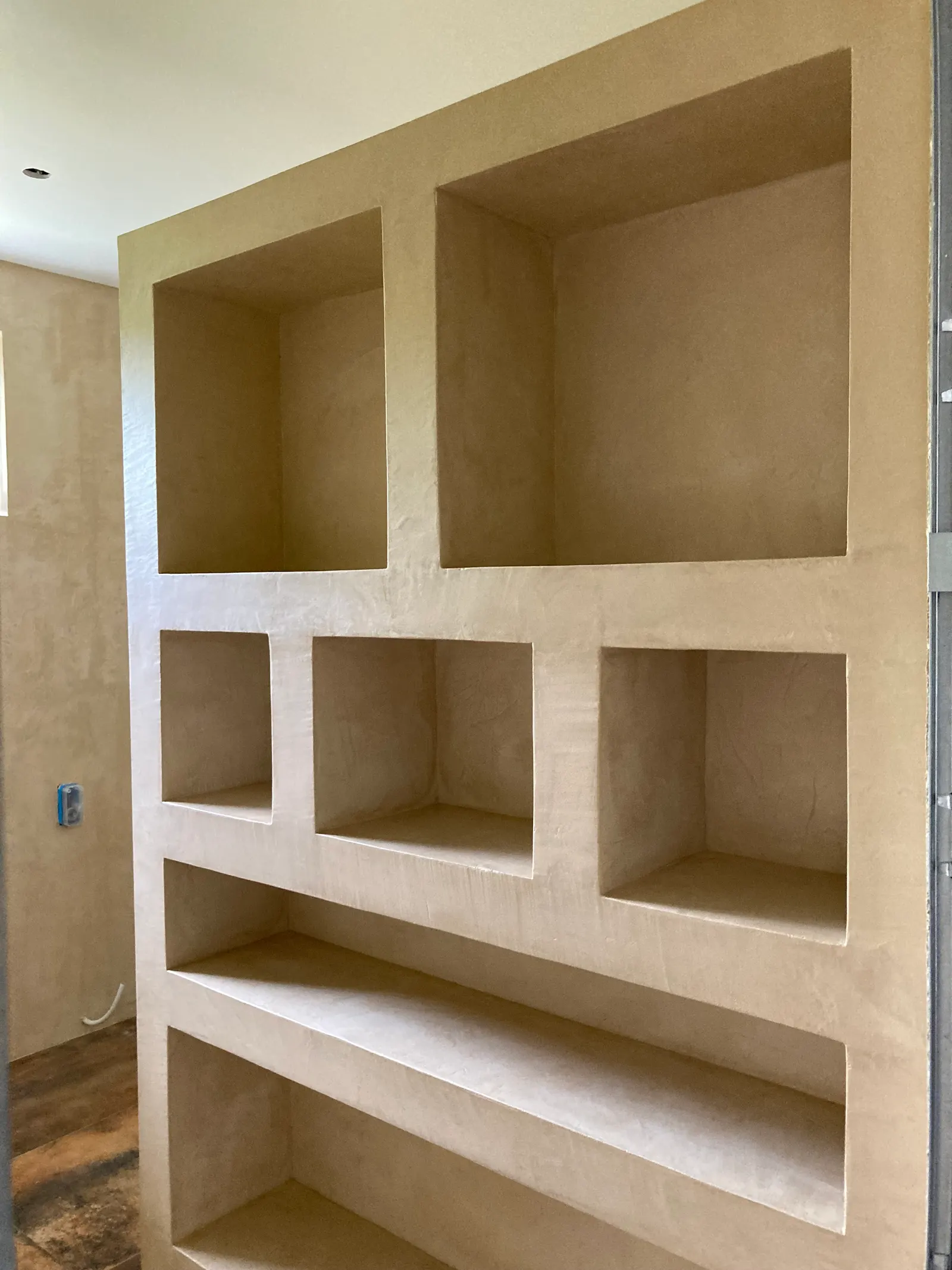 Bibliothèque maçonnée en béton ciré beige avec casiers de tailles différentes et étagères longues