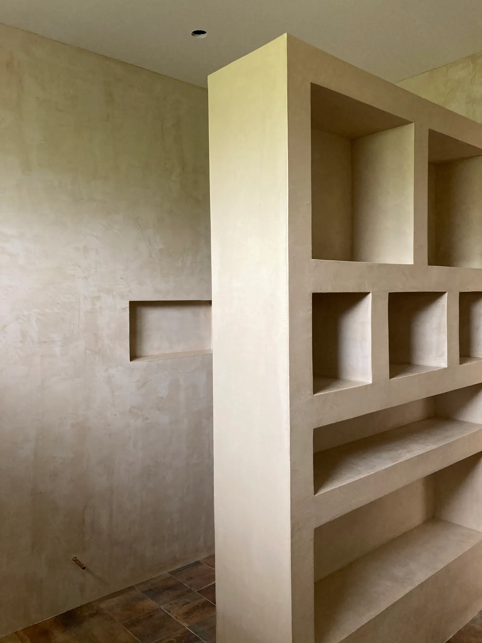 Vue de côté de la bibliothèque en béton ciré beige et du mur à niche horizontale
