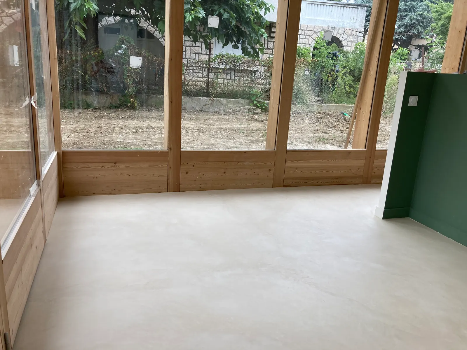 Sol en béton ciré blanc cassé dans une pièce vitrée à ossature bois, au pied des baies