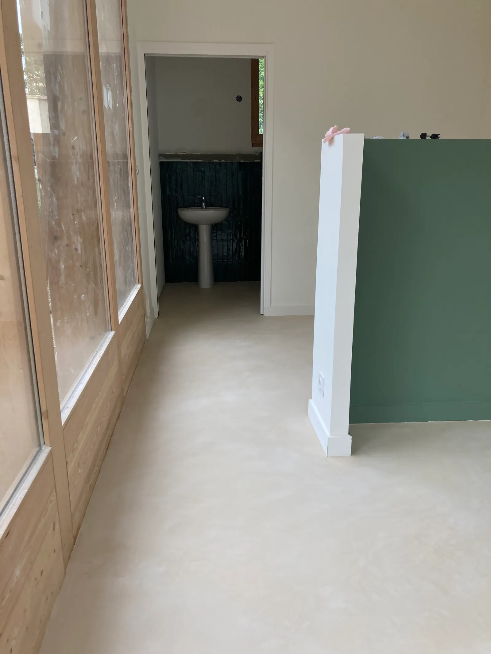 Sol en béton ciré clair qui longe les baies vitrées et se prolonge vers une salle d'eau