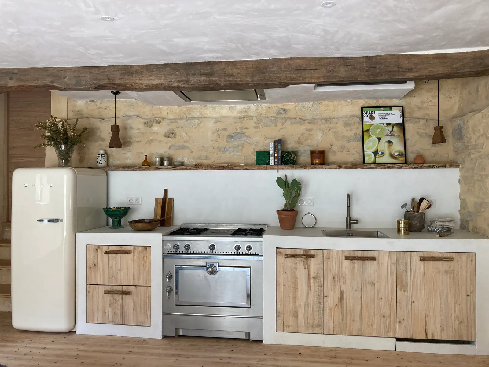 Cuisine maçonnée en béton ciré blanc avec façades en bois brut, crédence assortie et mur en pierre apparente