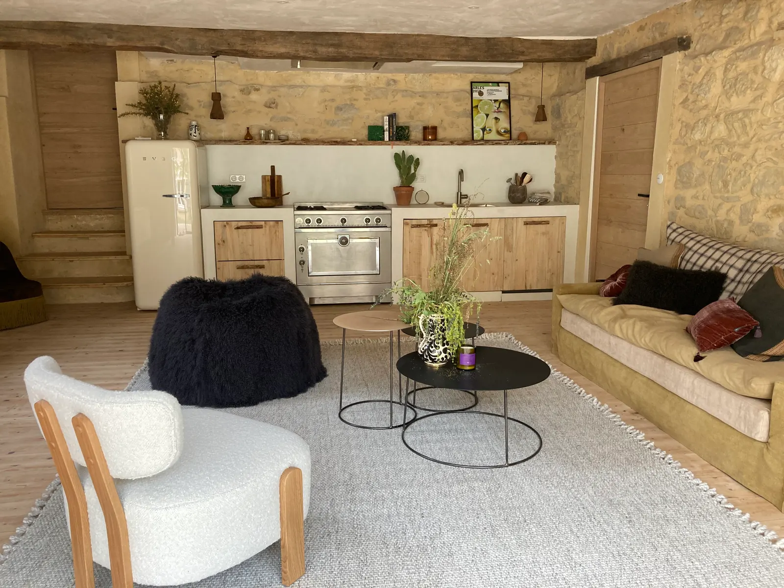 Vue d'ensemble de la pièce de vie avec la cuisine maçonnée en béton ciré blanc au fond, sous une poutre ancienne