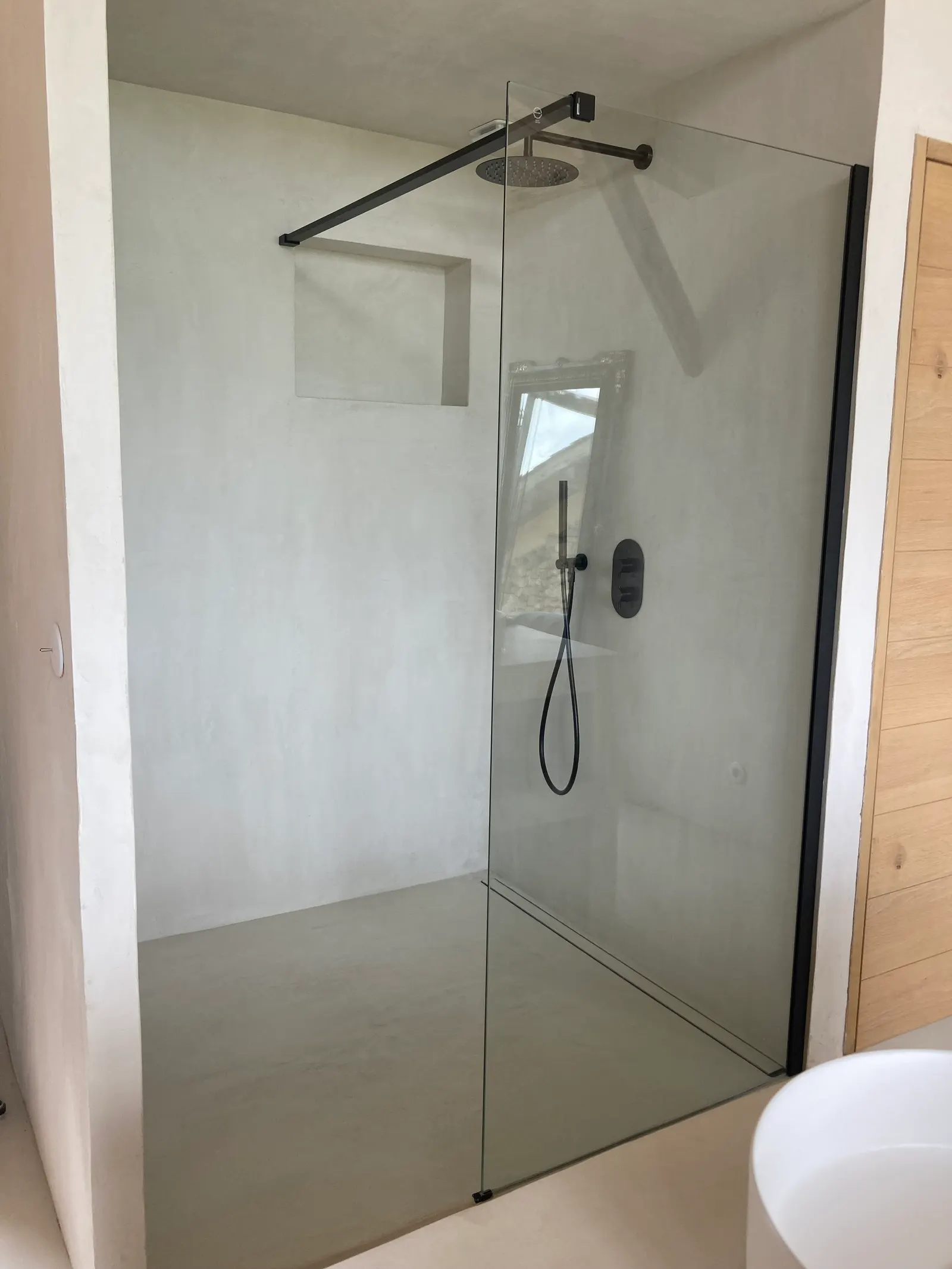 Douche à l'italienne en béton ciré gris clair avec niche murale, paroi vitrée fixe et robinetterie noire